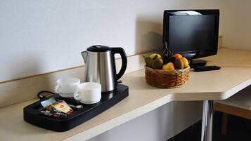 A hotel room with a coffee maker, two cups, a basket of fruit, and a television on a counter.