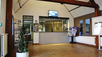 A reception area with a tiled floor, a reception desk, a television mounted above the desk, and a potted plant.