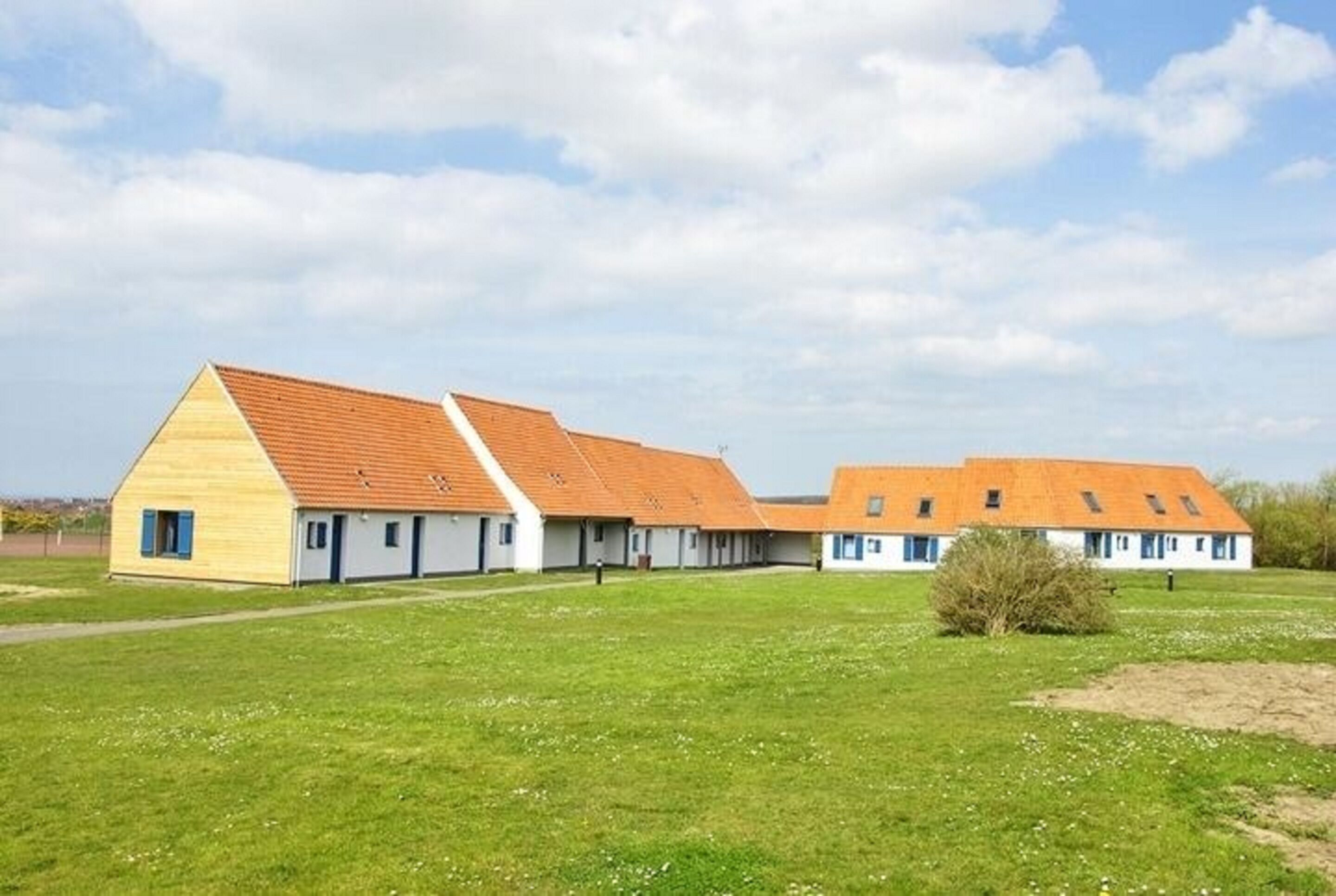 A row of white buildings with orange roofs and a grassy field in front.