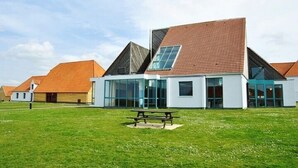 Un edificio moderno con techo inclinado, ventanas grandes y una mesa de picnic al frente.