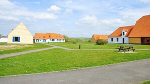 Un entorno rural con una gran estructura piramidal, varias construcciones tradicionales con tejados anaranjados y una mesa de picnic en un césped.