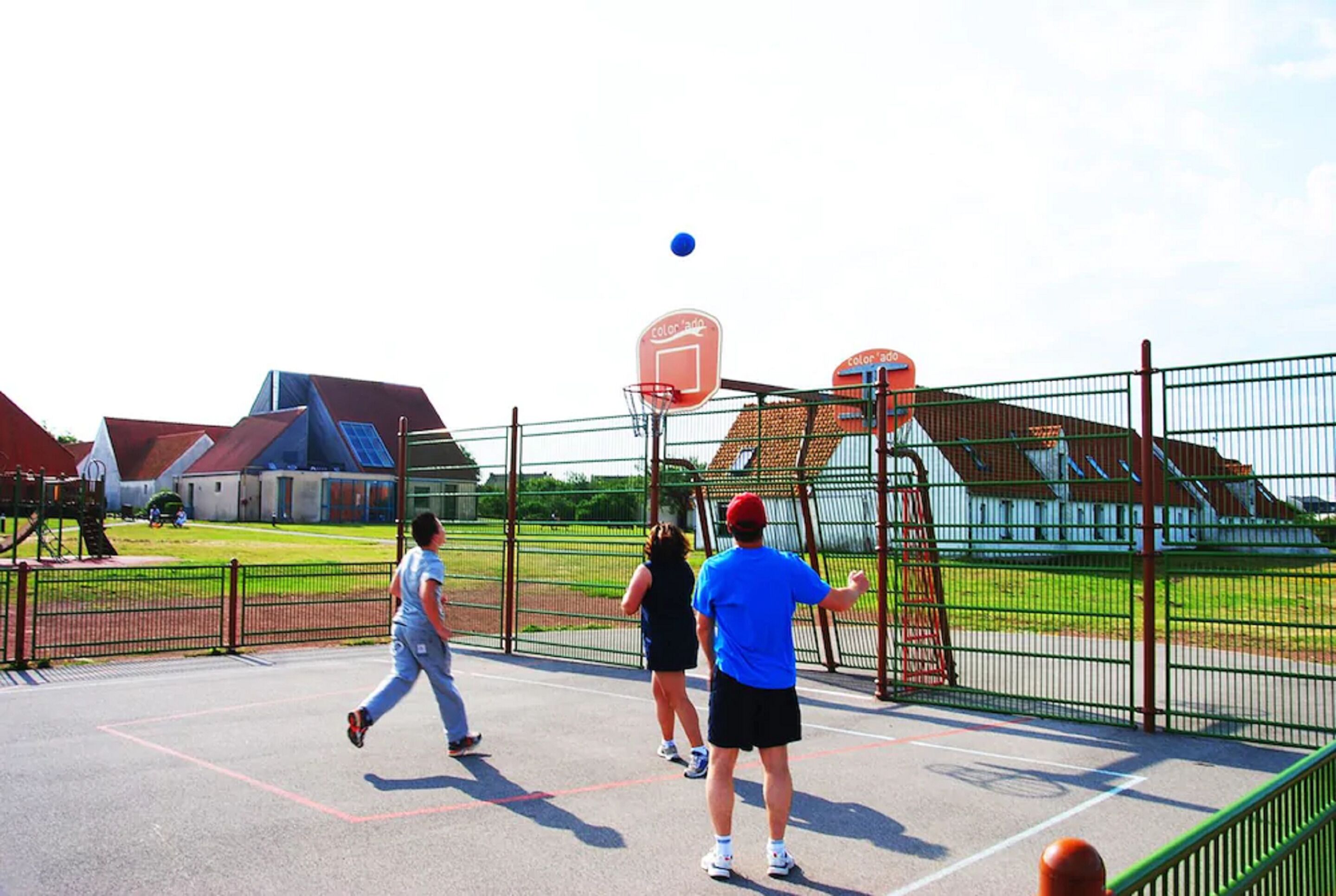 Ein Basketballplatz mit Netz, Zaun und einem Gebäude im Hintergrund.