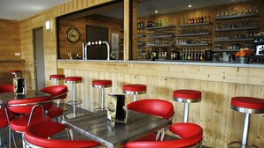Zona de bar con paredes de madera, taburetes rojos y una variedad de botellas y vasos en estantes.