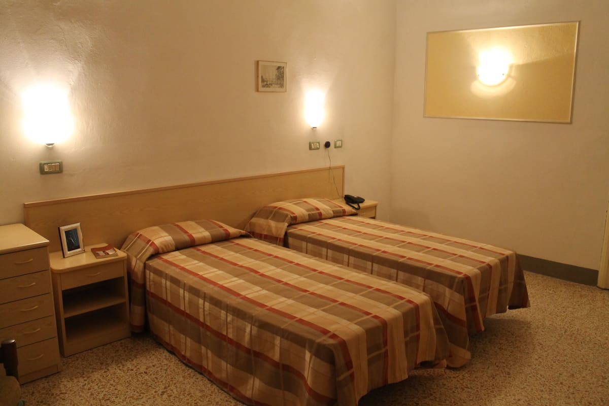 Une chambre d’hôtel avec deux lits, une table de chevet et une lampe fixée au mur.