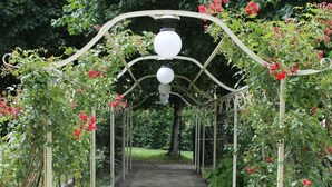 A pathway with a tiled floor, surrounded by greenery and red flowers, leading to a white structure. - Hotel Croce di Savoia (Reggello)