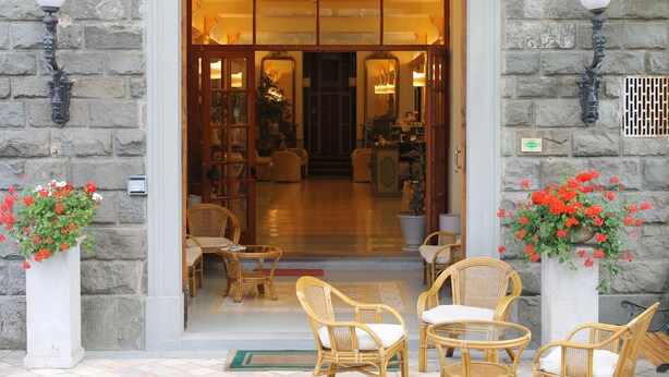 A hotel entrance with stone walls, a wooden door, wicker furniture, and flower pots. - Hotel Croce di Savoia (Reggello)