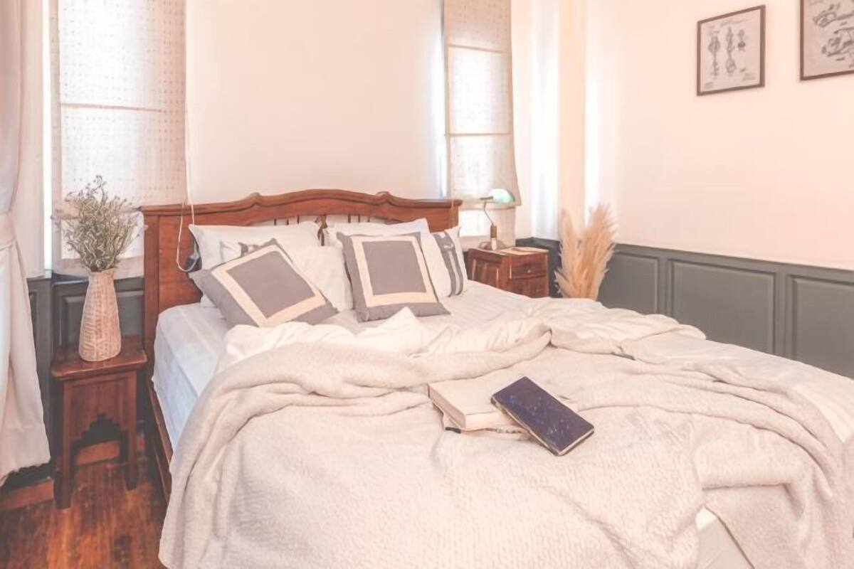 A neatly made bed with pillows, a bedside lamp, and a book on the bed.