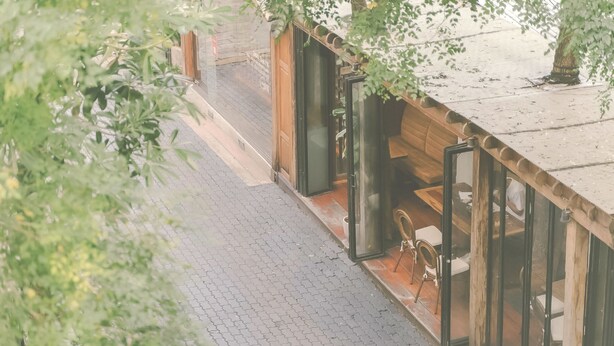 A modern building with a glass entrance, a wooden deck, and a seating area with a table and chairs. - Yesterday Hotel (Chiang Mai)