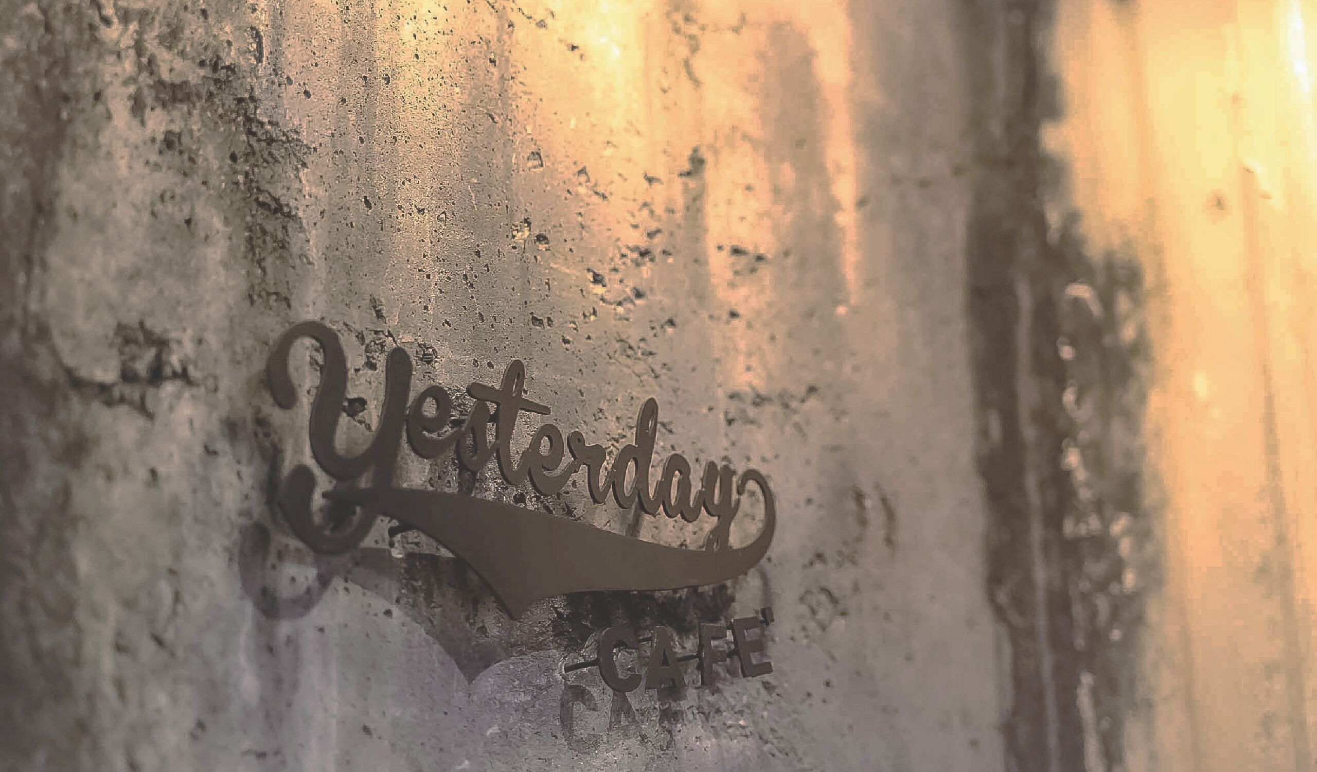 A metal sign with the word "Yesterday" and "CAFE" on a textured wall.