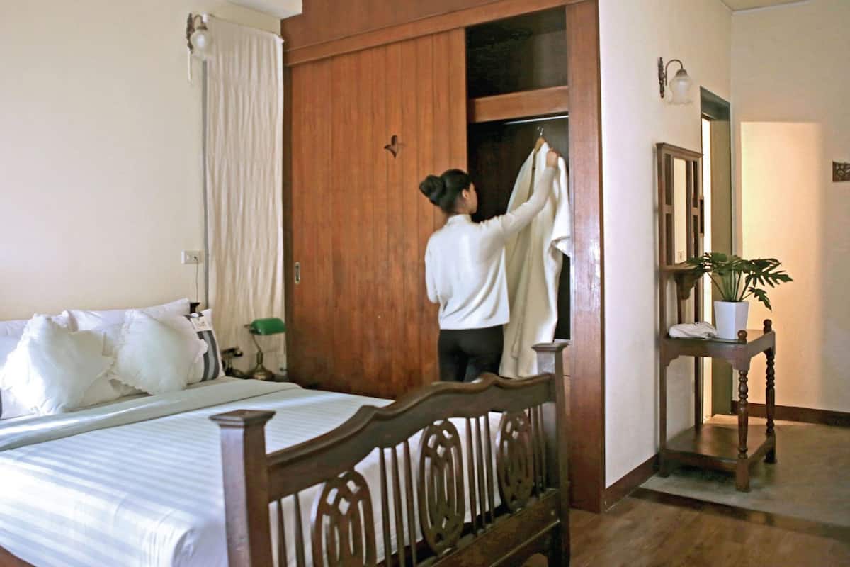A hotel room with a bed, a wooden wardrobe, a mirror, and a potted plant.