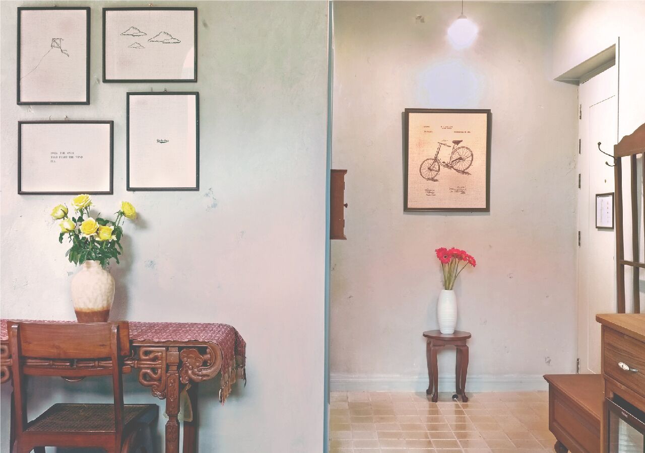 Een kamer met een eettafel, stoelen, een vaas met gele bloemen en een lijst met een afbeelding van een fiets aan de muur.