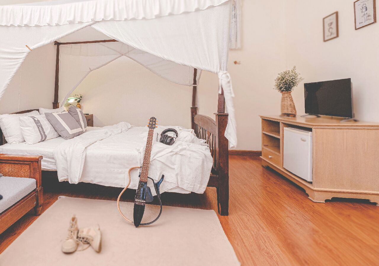 A bedroom with a canopy bed, a guitar, a TV, and a small cabinet.