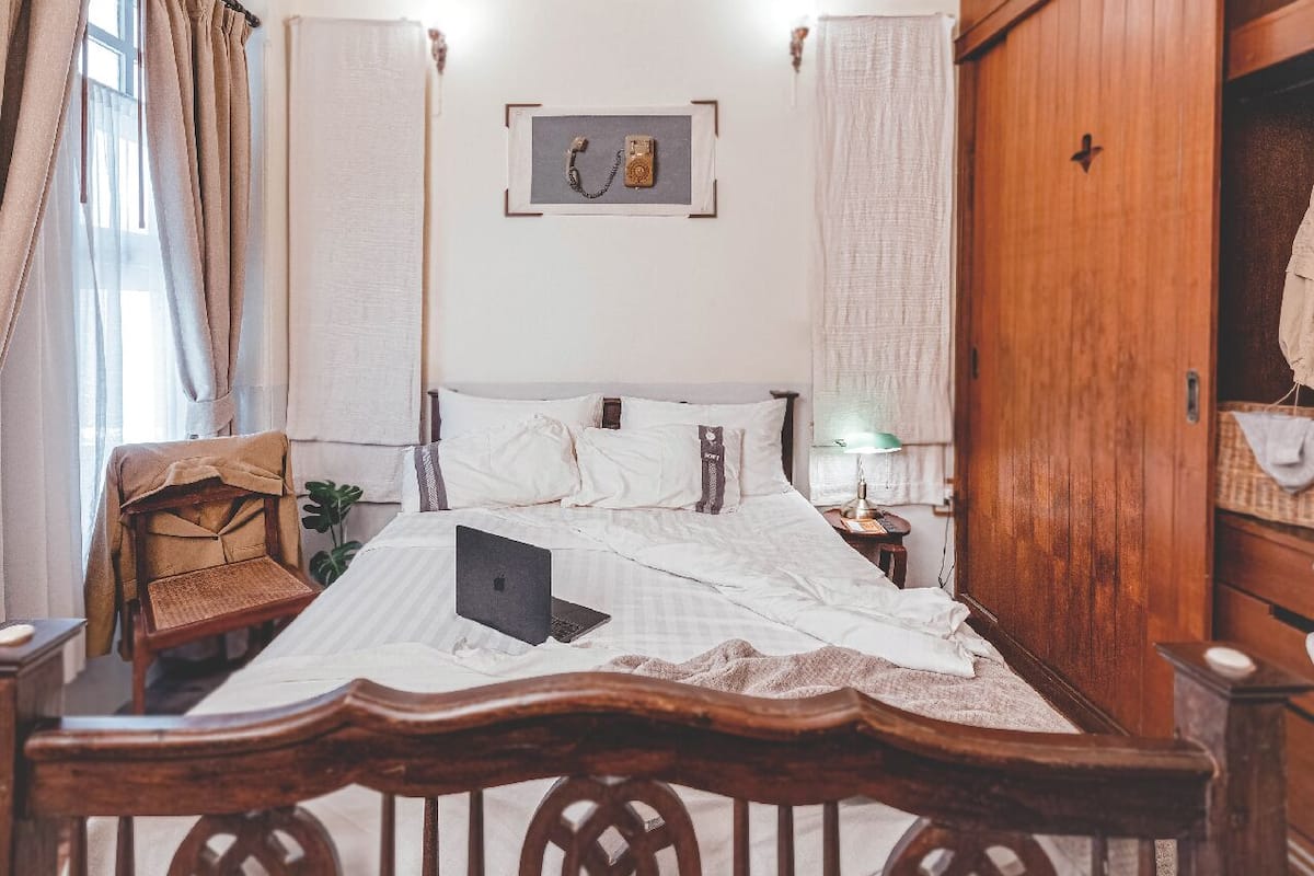 A bedroom with a bed, a laptop on the bed, a wooden wardrobe, and a framed picture on the wall.