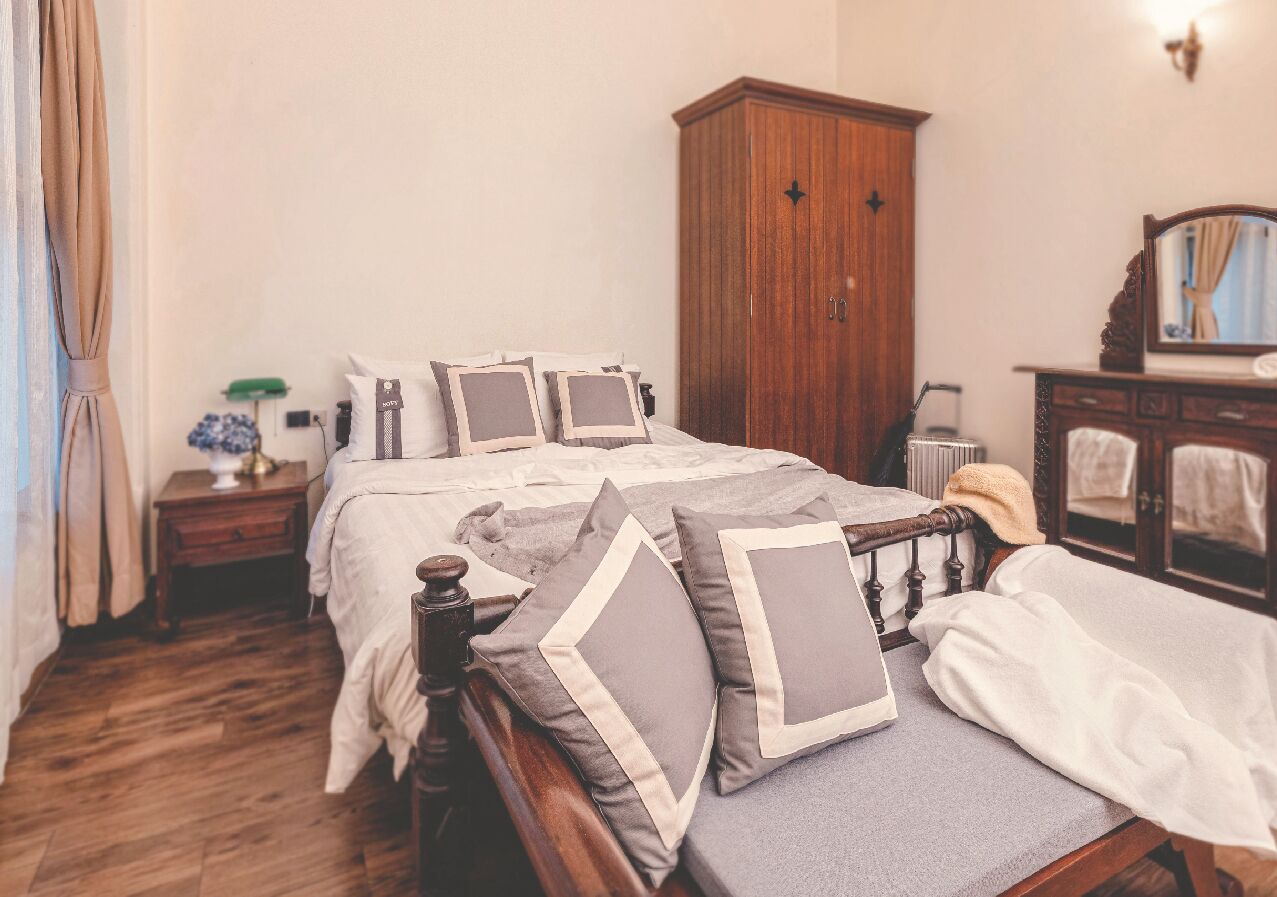 A bedroom with a wooden bed, a nightstand, a wardrobe, and a mirror.