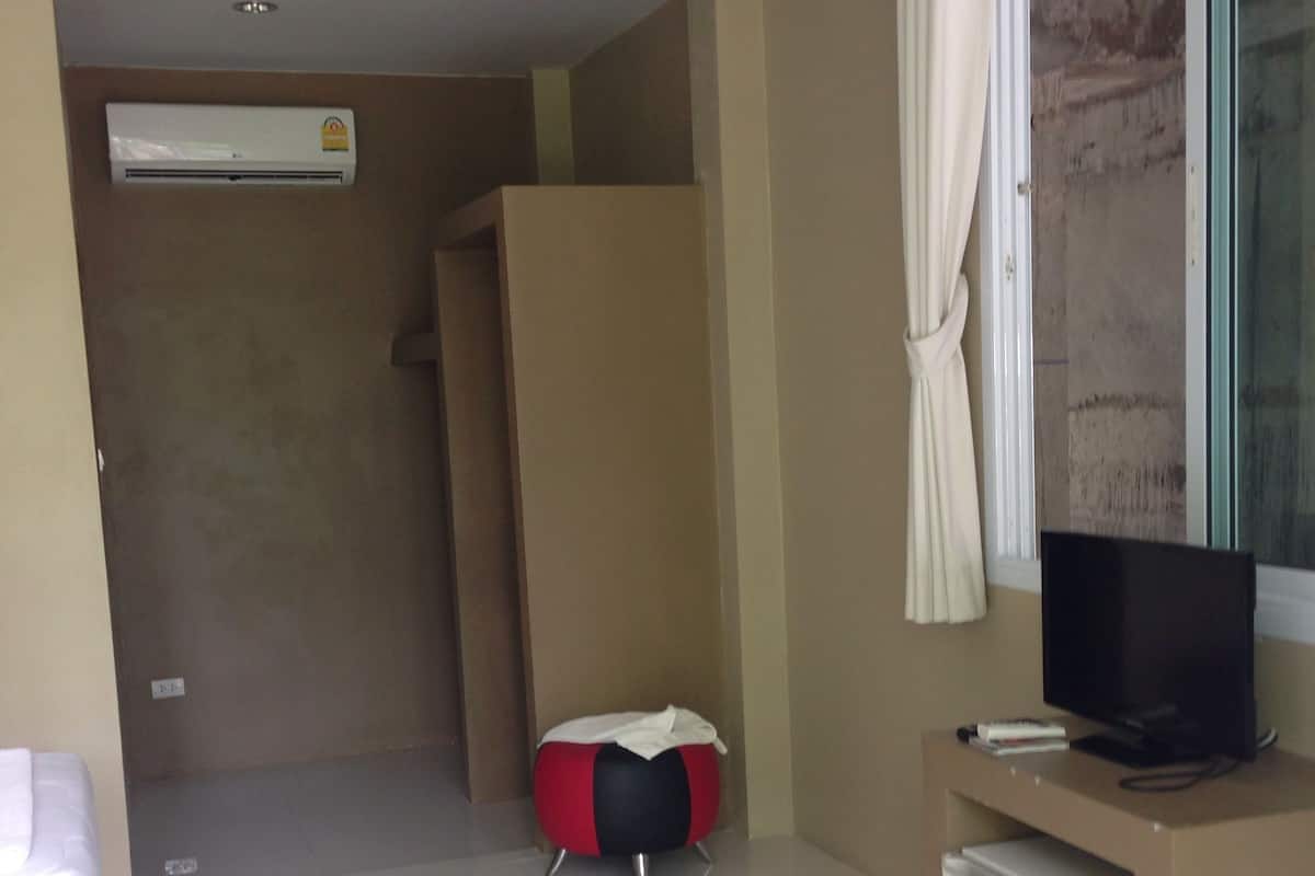 Habitación de hotel con cama, un televisor pequeño sobre un soporte, un refrigerador minibar y un otoman rojo y negro.