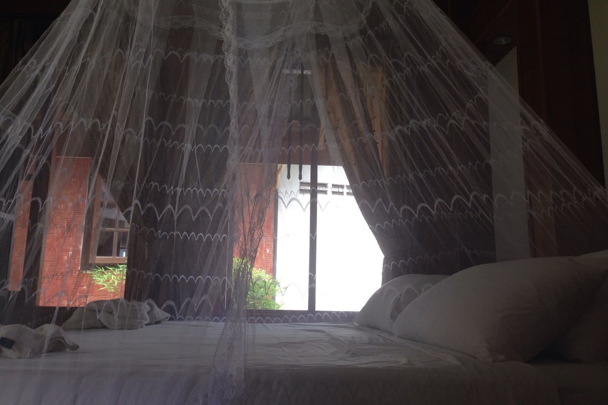 Una cama con dosel, una ventana y vista a zonas verdes.