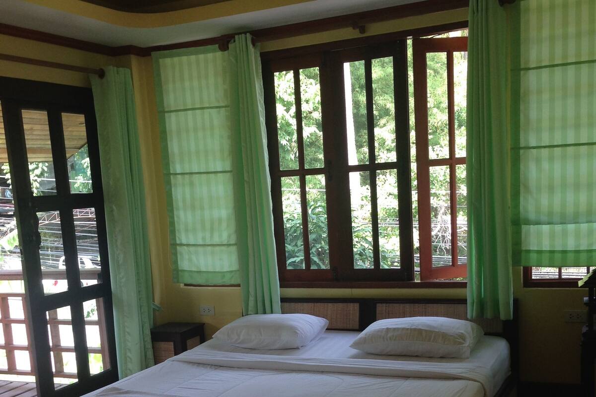Una cama bien hecha con sábanas blancas en una habitación con un ventanal y cortinas verdes.