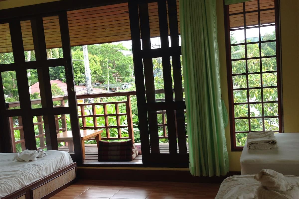 Una habitación con dos camas, vista al verdor exterior y un balcón con baranda de madera.