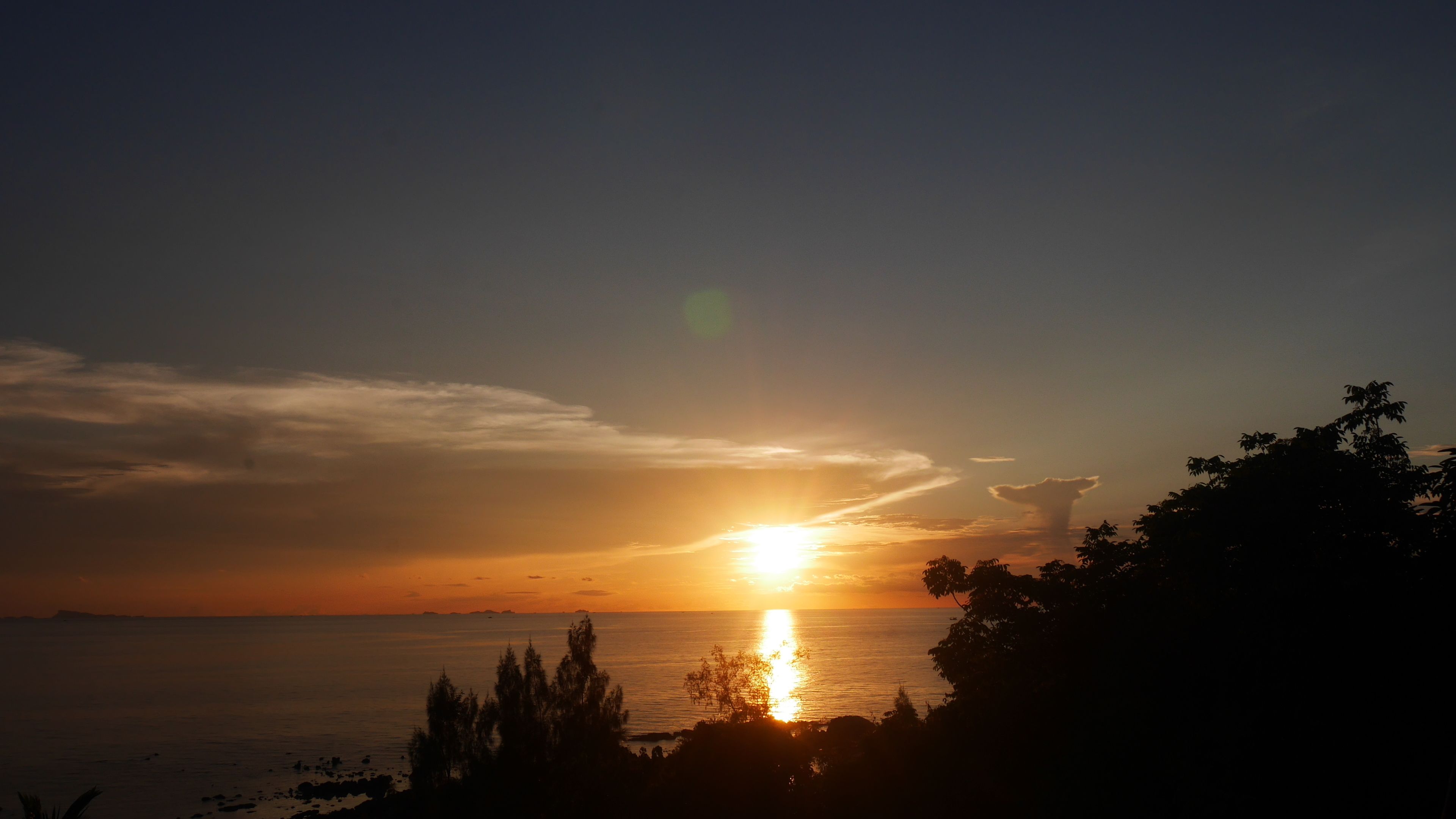A sunset over a body of water with silhouettes of trees and a clear sky.