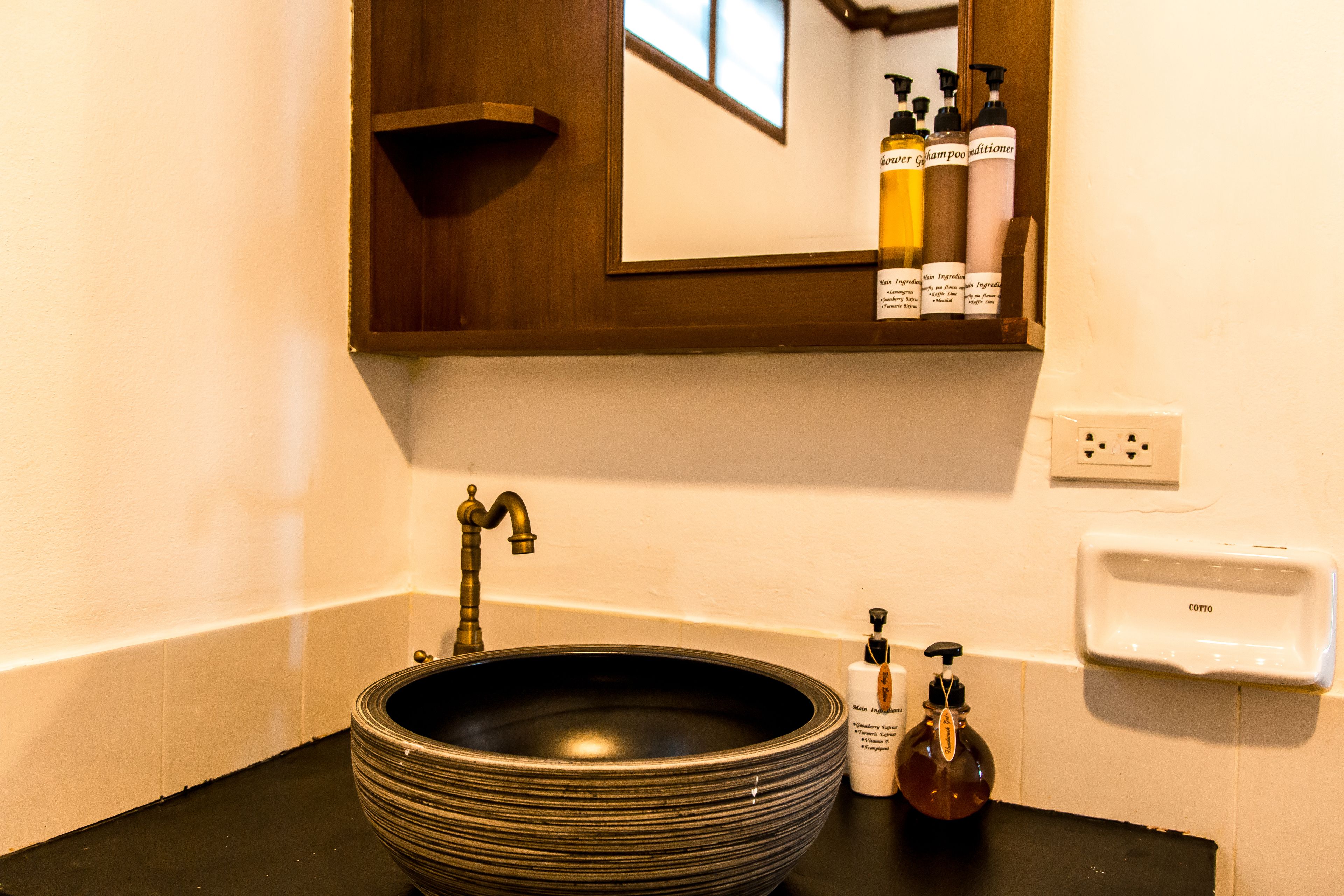 A bathroom with a large, ribbed vessel sink, a mirror above it, and a shelf with toiletries.