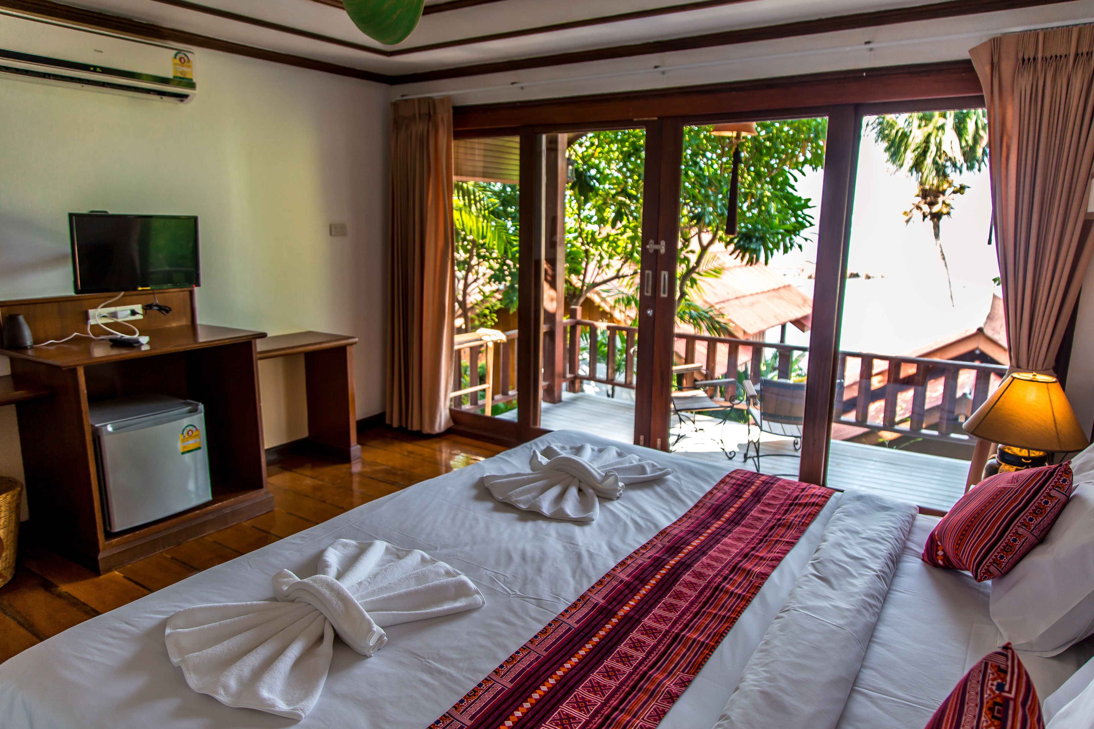 Quarto de hotel com cama, escrivaninha com computador, televisão e pequeno frigorífico.