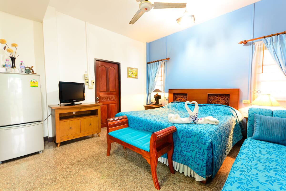 Une chambre d’hôtel équipée d’un lit, d’un banc en bois, d’une télévision, d’un réfrigérateur et d’un ventilateur de plafond.