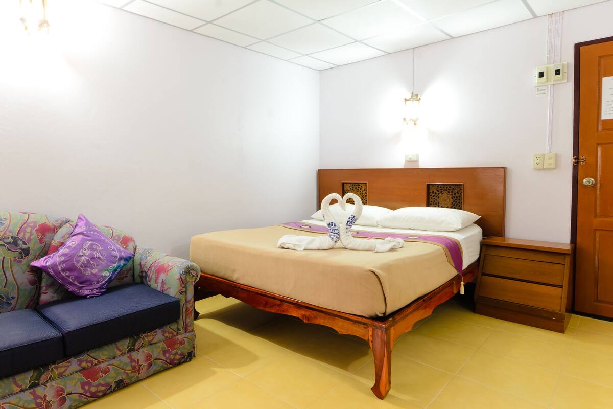Une chambre d’hôtel avec un lit, un canapé, une table de chevet en bois et une porte.