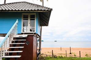 Uma casa de praia com fachada azul, telhado telhado e escadaria que dá para uma varanda.