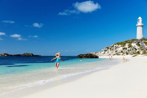 A beach with a lighthouse, clear blue water, and rocky outcrops. - Stay Rottnest (Rottnest Island)