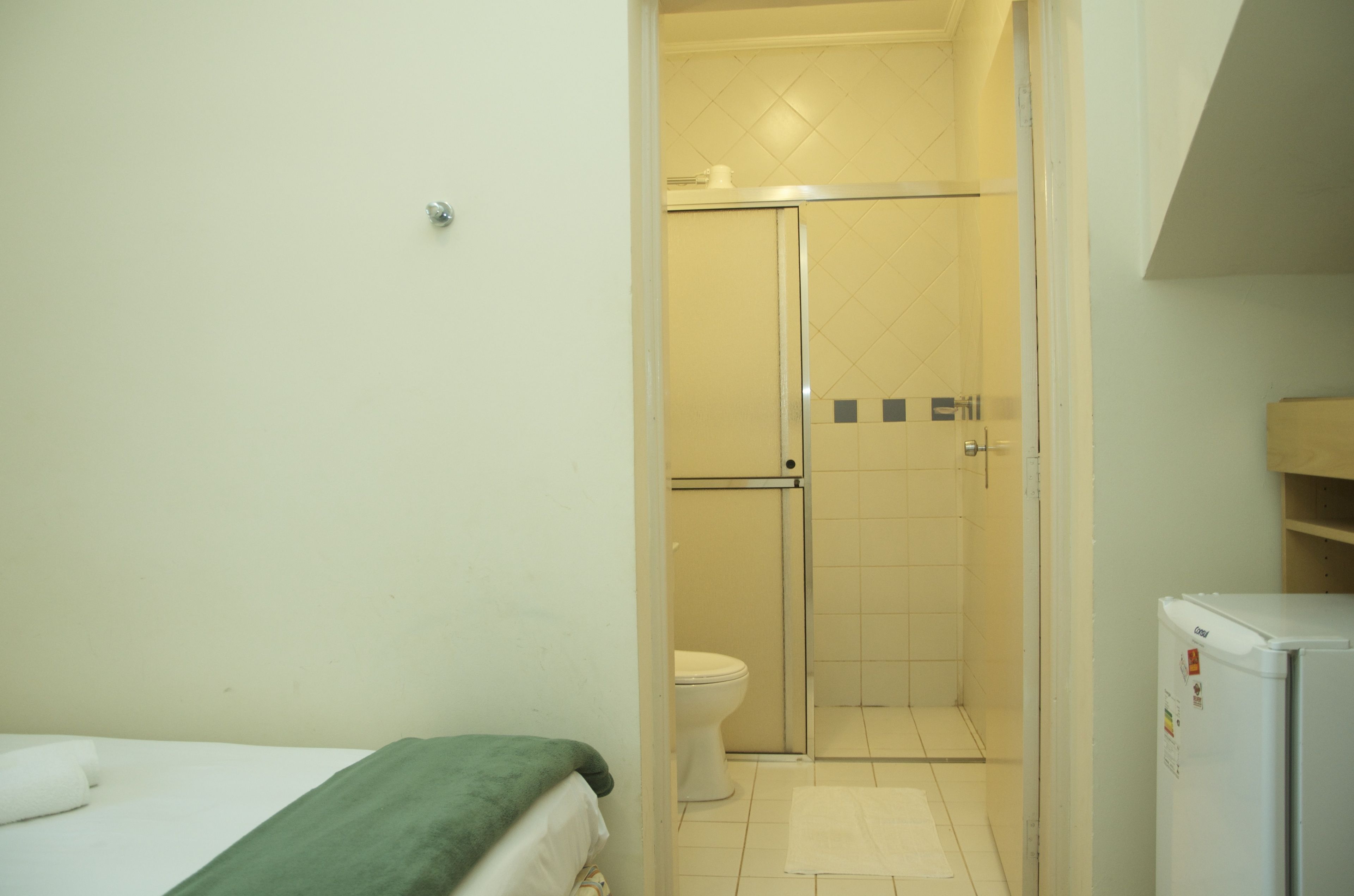 A small, clean bathroom with a shower, toilet, and a refrigerator.