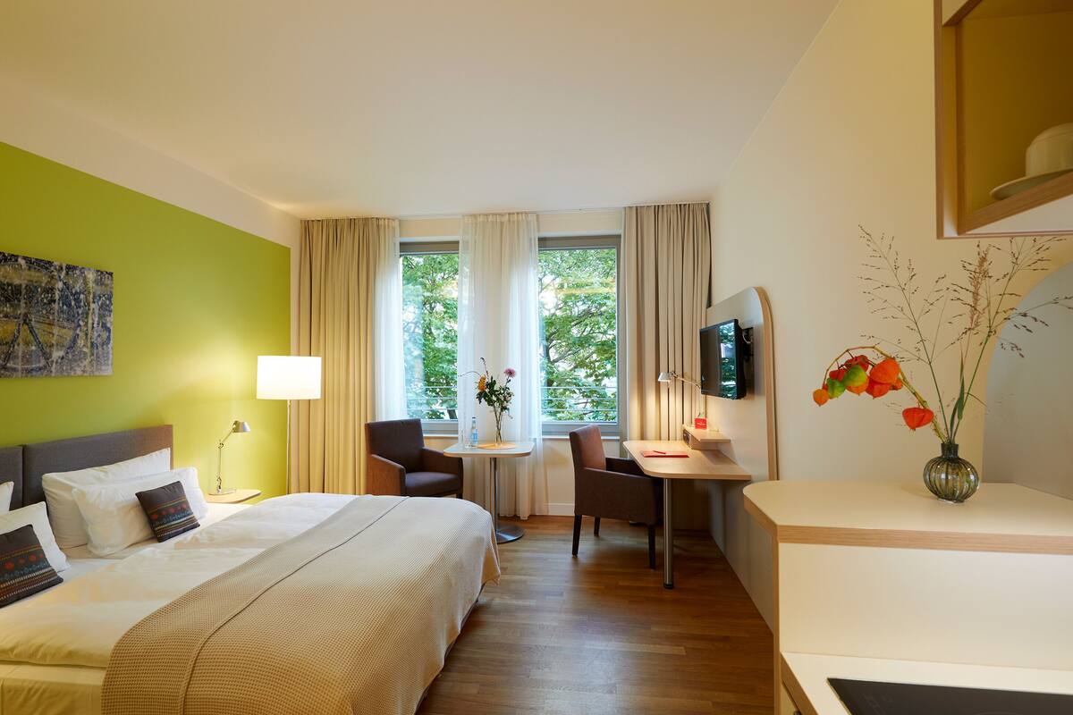 A hotel room with a bed, a desk, a chair, a TV, and a window with curtains.