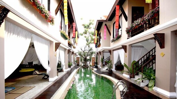 An indoor swimming pool with a central water feature, surrounded by balconies with plants and flowers. - Devara Pool Villa (Pattaya)