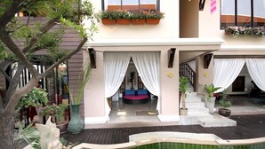 A two-story building with a covered outdoor area featuring a small pool, potted plants, and a seating area with cushions. - Devara Pool Villa (Pattaya)