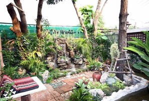 Stroll through the serene garden, featuring a small waterfall and lush greenery, with a wooden ladder leading to a raised platform.