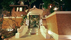 A well-lit entrance with a covered walkway, a brick wall, and a tree-lined path leading to a building. - Devara Pool Villa (Pattaya)
