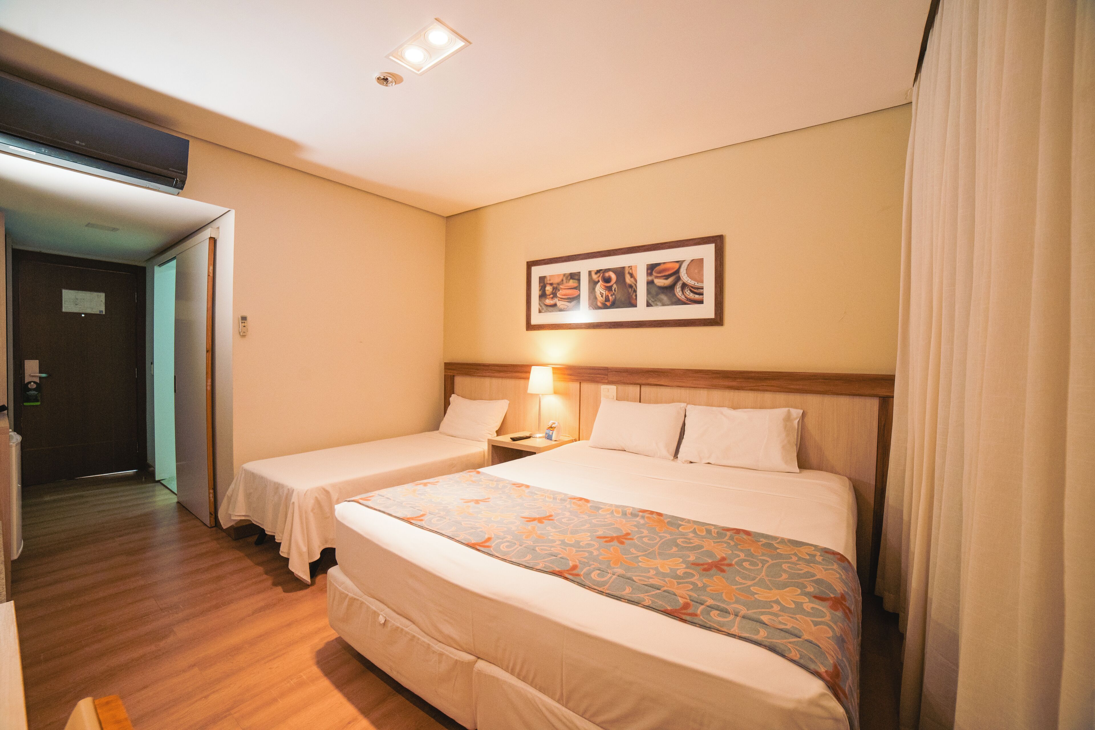 Une chambre d’hôtel avec deux lits, une tête de lit en bois, une table de chevet avec une lampe et un tableau encadré au mur.