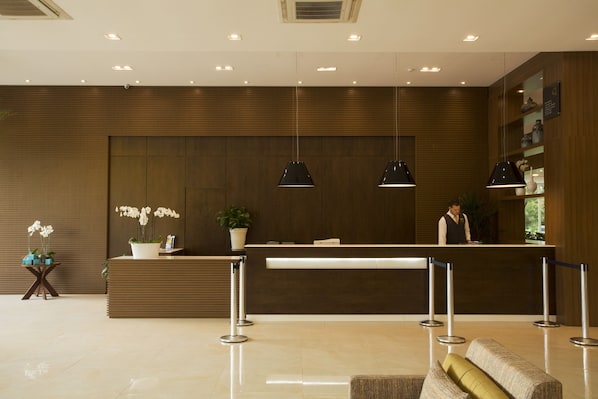A modern reception area with a wooden reception desk, potted plants, and a receptionist.