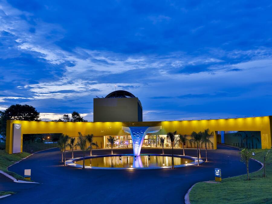 A modern building with a circular water feature in front, a prominent yellow facade, and a dome structure in the background.