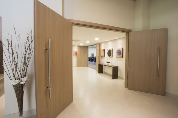 Un moderno vestíbulo de hotel con puertas de madera, un mostrador de recepción y un jarrón con ramas.