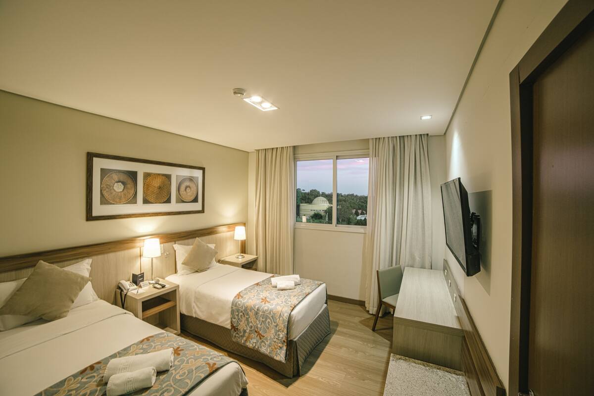 Een hotelkamer met twee bedden, een televisie, een bureau met lamp en een raam met gordijnen.