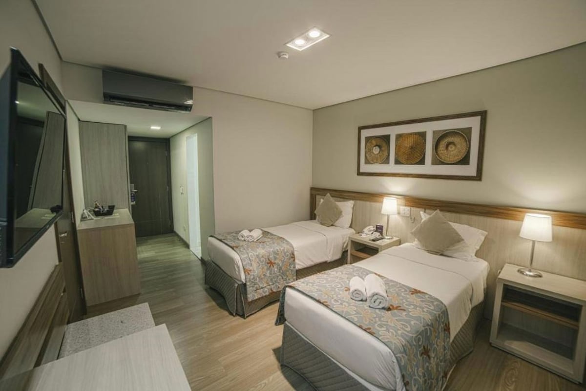 Habitació d'hotel amb dos llits, una taula de treball, un mirall i una obra d'art penjada a la paret.
