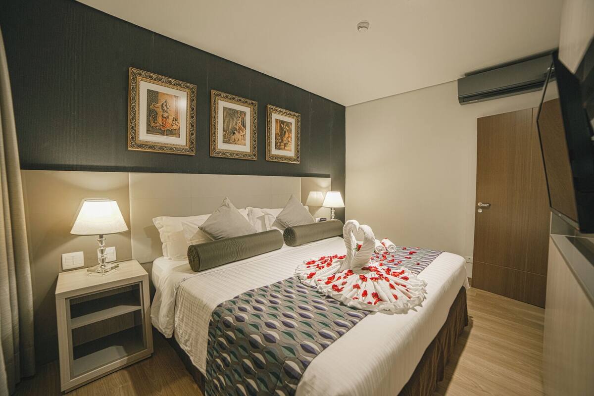 Een hotelkamer met een bed, twee nachtkastjes met lampen, een garderobe en drie ingelijste foto’s aan de muur.