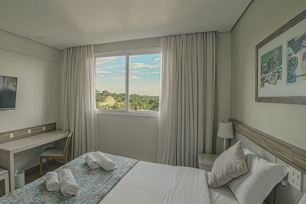 Habitació d'hotel amb un llit, escriptori, cadira, televisió i finestra amb cortines.