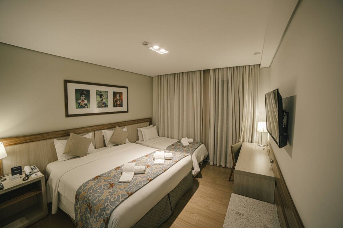 Een hotelkamer met twee bedden, een bureau, een televisie en een ingelijst schilderij aan de muur.