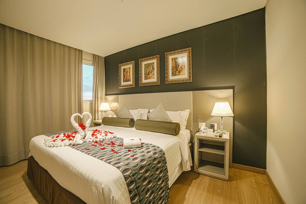 Een hotelkamer met een groot bed, twee nachtkastjes, een raam met gordijnen en drie ingekaderde foto's aan de muur.