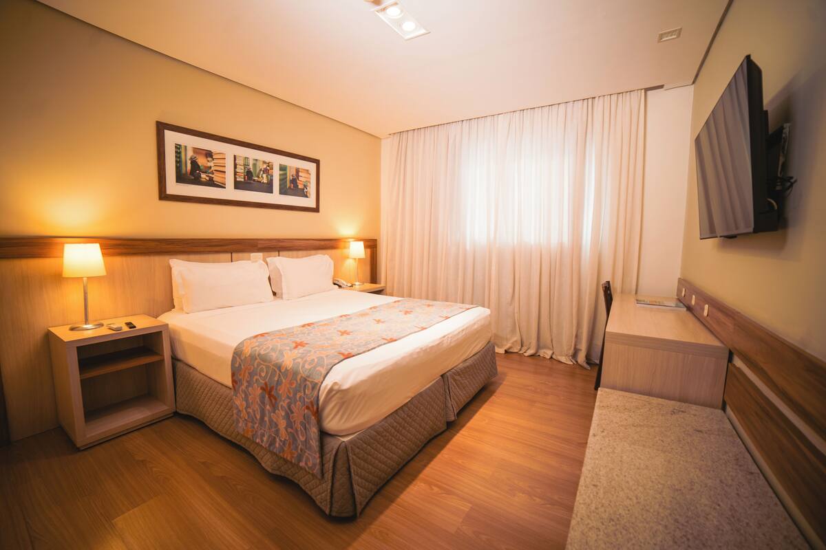 Een hotelkamer met een bed, nachtkastjes, een televisie en een raam met gordijnen.