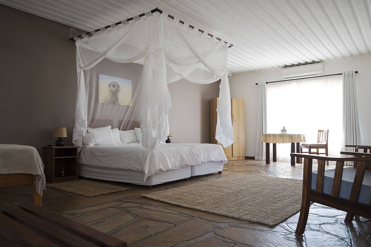 A bedroom with a four-poster bed, a wooden nightstand, a table with a lamp, and a chair.