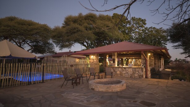 An outdoor patio area with a stone fire pit, lounge chairs, and a pool. - Dornhügel Guestfarm (Grootfontein)
