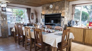 A dining area with a stone fireplace, wooden chairs, and a tiled floor. - Dornhügel Guestfarm (Grootfontein)