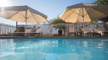 Una piscina al aire libre, sombrillas, sillones reclinables de piscina